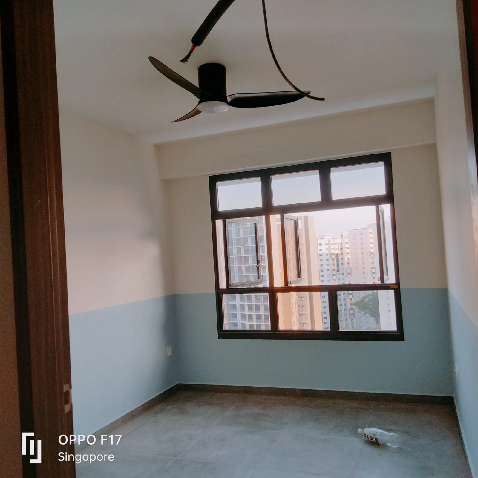 A freshly painted modern condo room featuring a two-tone blue and white wall, a black ceiling fan, and large framed windows overlooking city high-rises.