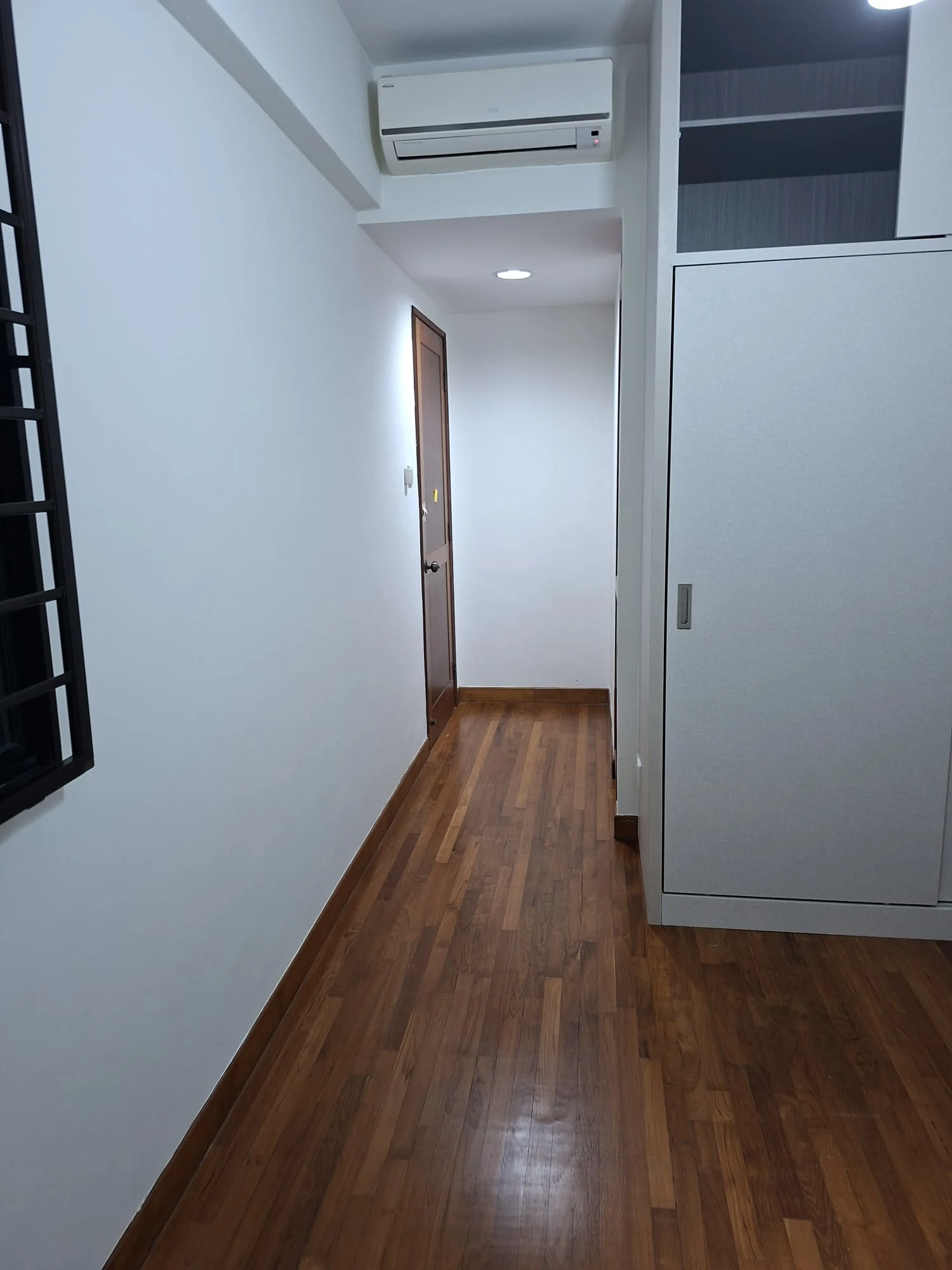 A freshly repainted modern hallway featuring crisp white walls, rich hardwood floorboards, a wall-mounted air conditioner, and built-in white cabinetry.