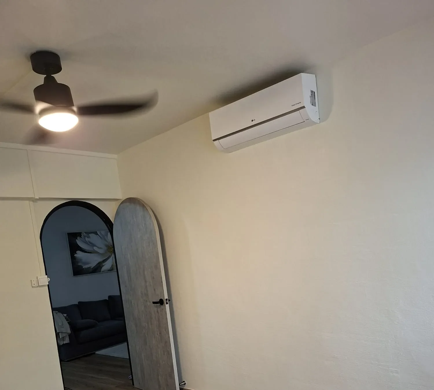 Freshly painted cream-colored room featuring an arched doorway, light wood door, wall-mounted air conditioner, and black ceiling fan.