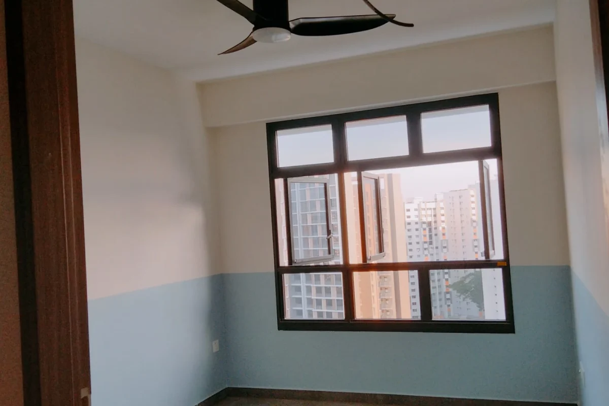 A freshly painted modern condo room featuring a two-tone blue and white wall, a black ceiling fan, and large framed windows overlooking city high-rises.