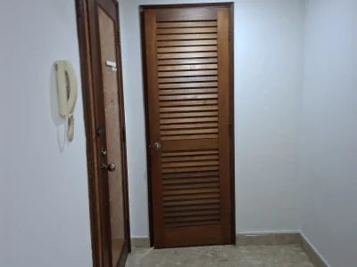 An indoor hallway featuring white walls, a wooden louvre door at the end, and a wooden entrance door on the left.
