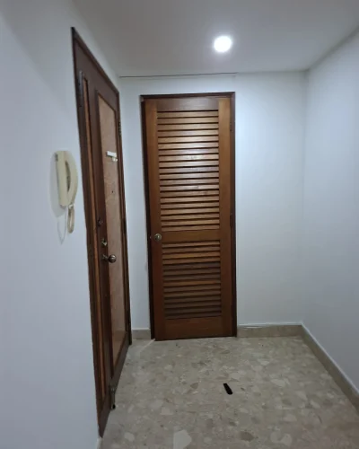 An indoor hallway featuring white walls, a wooden louvre door at the end, and a wooden entrance door on the left.