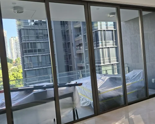 A modern living room with large glass sliding doors opening to a balcony with protected outdoor furniture and a view of high-rise city buildings.