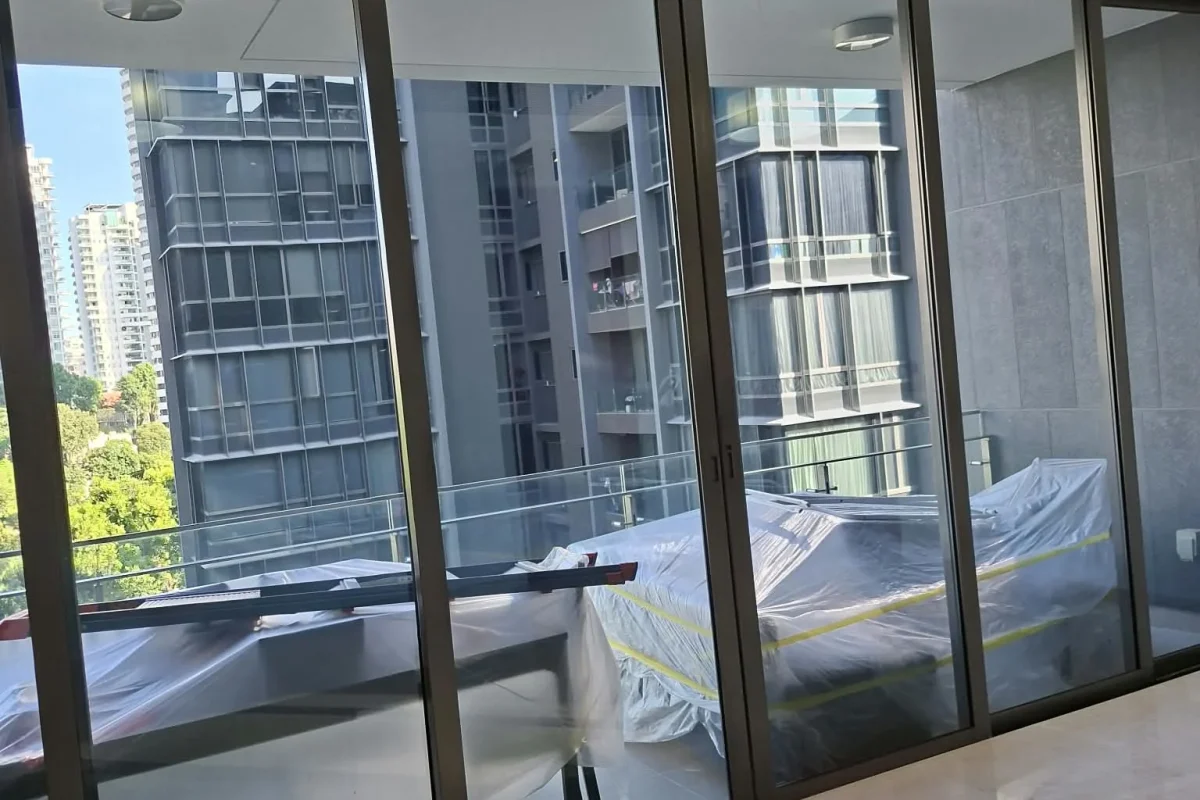 A modern living room with large glass sliding doors opening to a balcony with protected outdoor furniture and a view of high-rise city buildings.