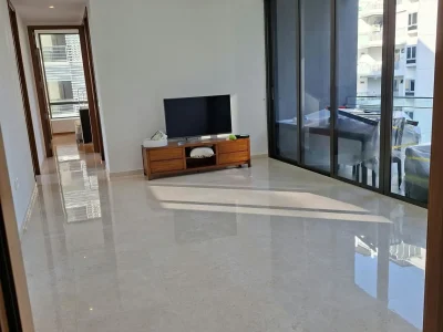 A spacious, brightly lit modern living room with polished marble floors, clean white walls, a TV media console, and large floor-to-ceiling glass sliding doors.
