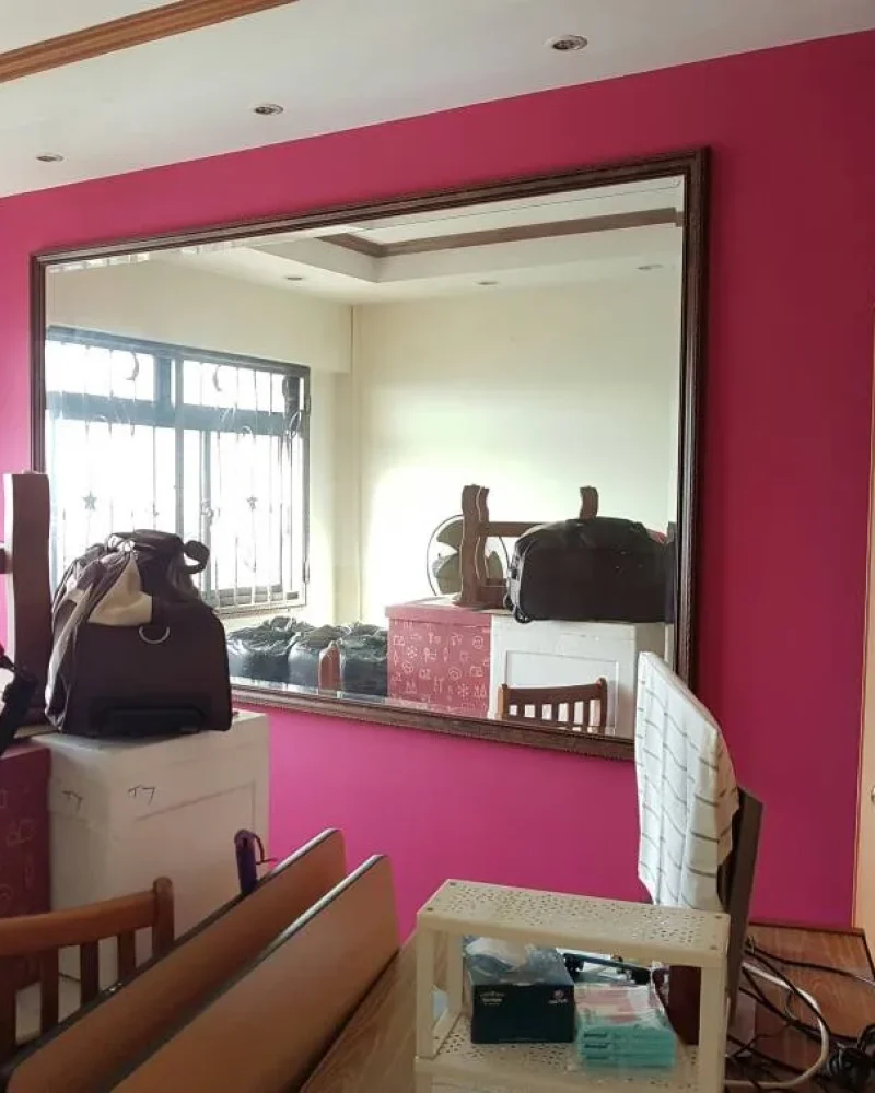 Interior view of a room with vibrant magenta accent wall, large framed mirror reflecting the room, recessed ceiling lights, and white ceiling in Singapore.