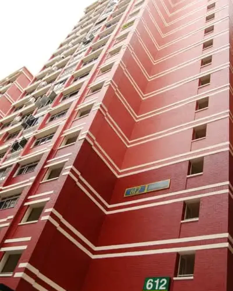 Low-angle view of a tall, red HDB residential apartment building in Singapore with white horizontal stripes and block number 612.