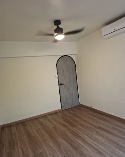 An interior room featuring freshly painted cream-white walls, wood-plank vinyl flooring, an arched grey door with a black frame, and a ceiling fan with light.