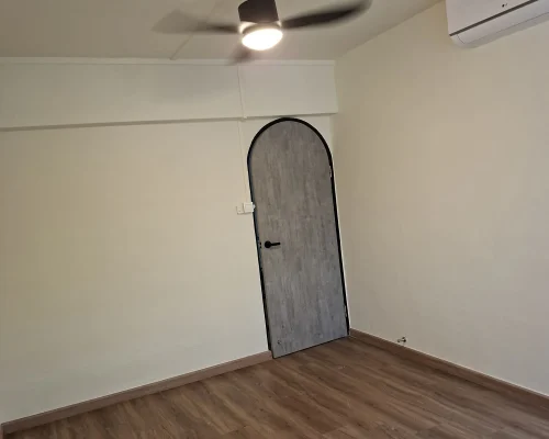 An interior room featuring freshly painted cream-white walls, wood-plank vinyl flooring, an arched grey door with a black frame, and a ceiling fan with light.