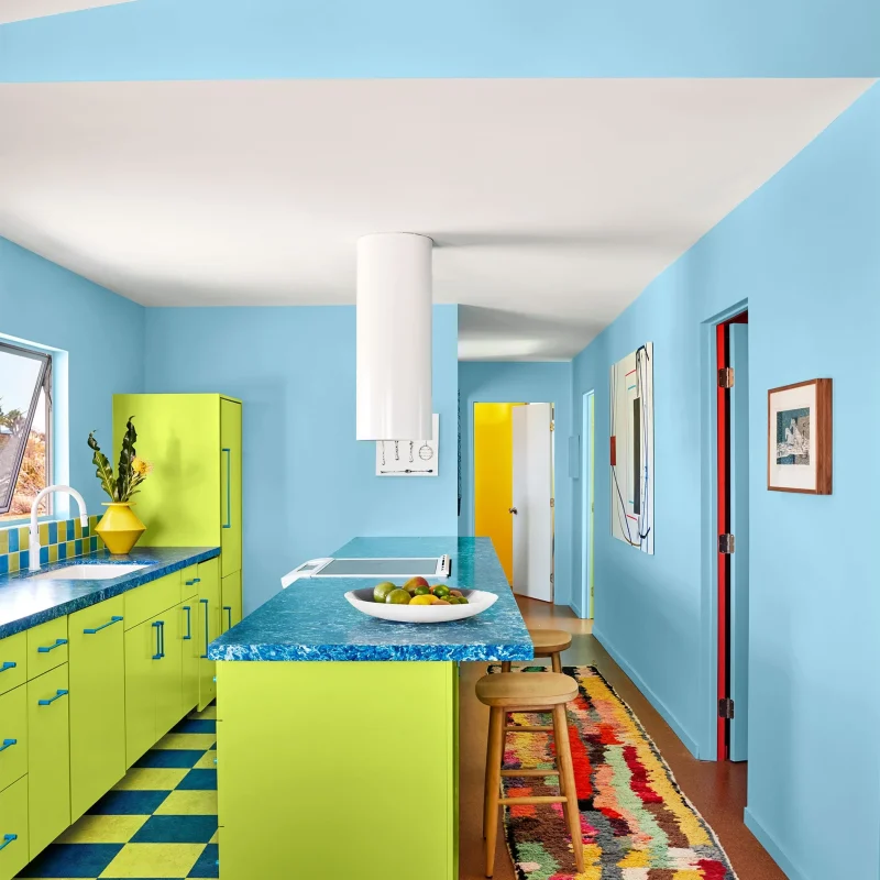 Bright modern kitchen featuring light blue painted walls, lime green cabinetry, blue textured countertops, and a colourful runner rug.