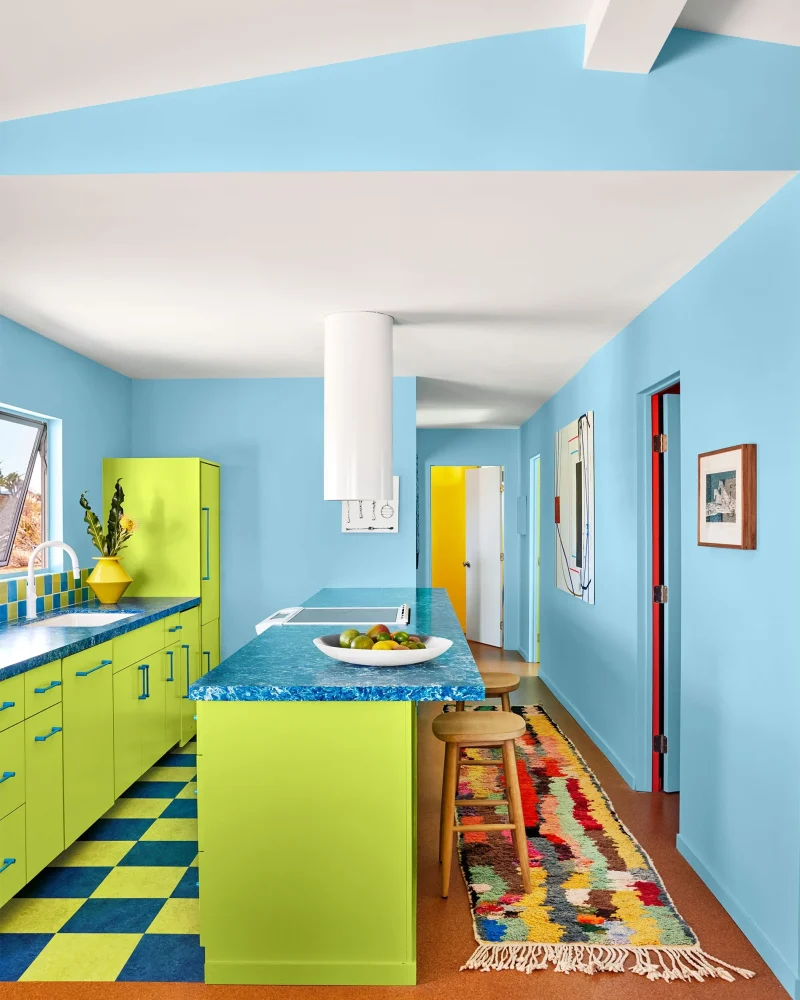 Bright modern kitchen featuring light blue painted walls, lime green cabinetry, blue textured countertops, and a colourful runner rug.