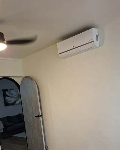 Freshly painted cream-colored room featuring an arched doorway, light wood door, wall-mounted air conditioner, and black ceiling fan.