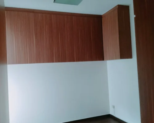 An interior room featuring upper wood-grain cabinets mounted against crisp white walls and dark wooden flooring.