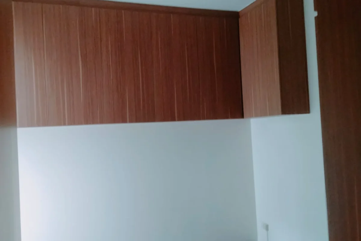 An interior room featuring upper wood-grain cabinets mounted against crisp white walls and dark wooden flooring.